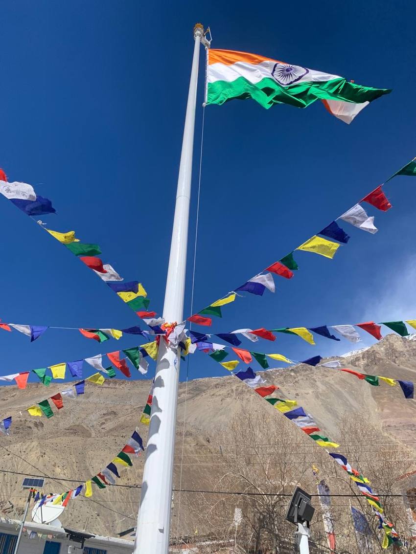 The Indian flag and prayer flags against a deep blue sky